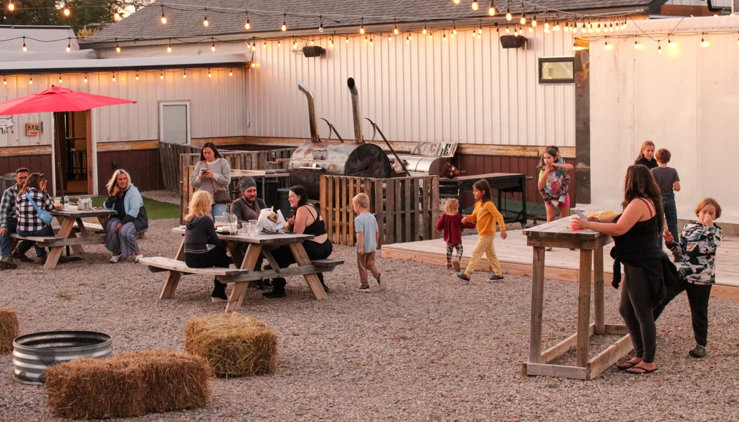 Dual-stack whole-hog offset smoker, outdoor kitchen sign and wooden second stage on the Iron Pig backyard patio