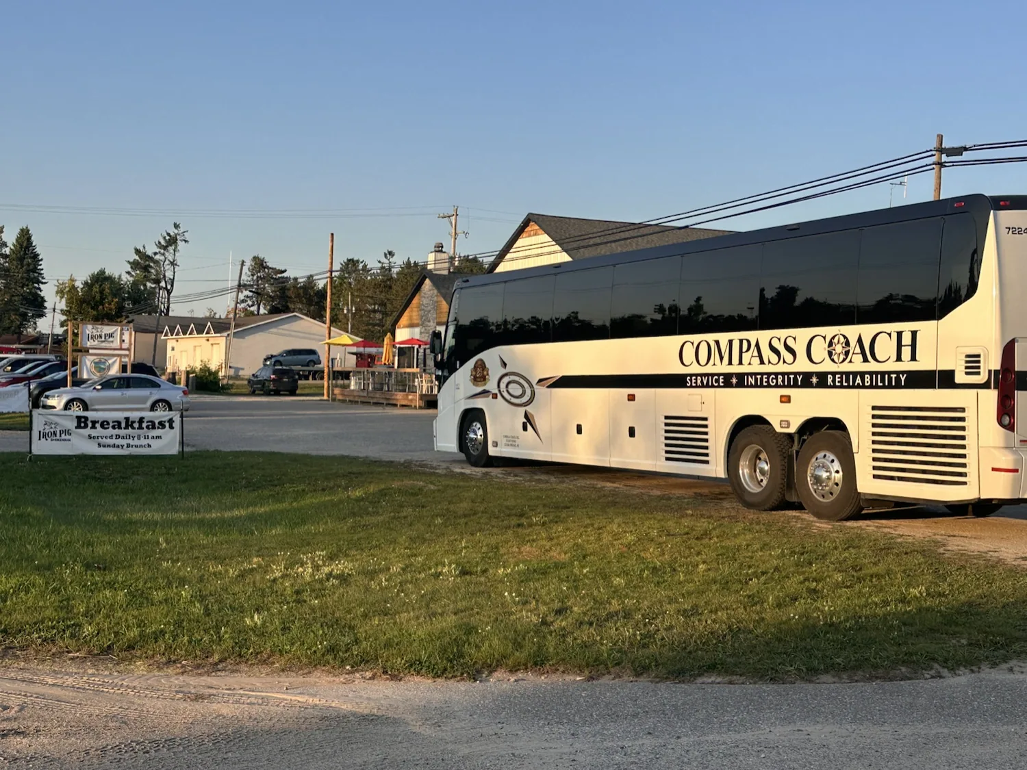 Full-size Compass Coach charter shuttle bus parked out front in front of the Iron Pig Smokehouse and The Lakeside Pavilion sign