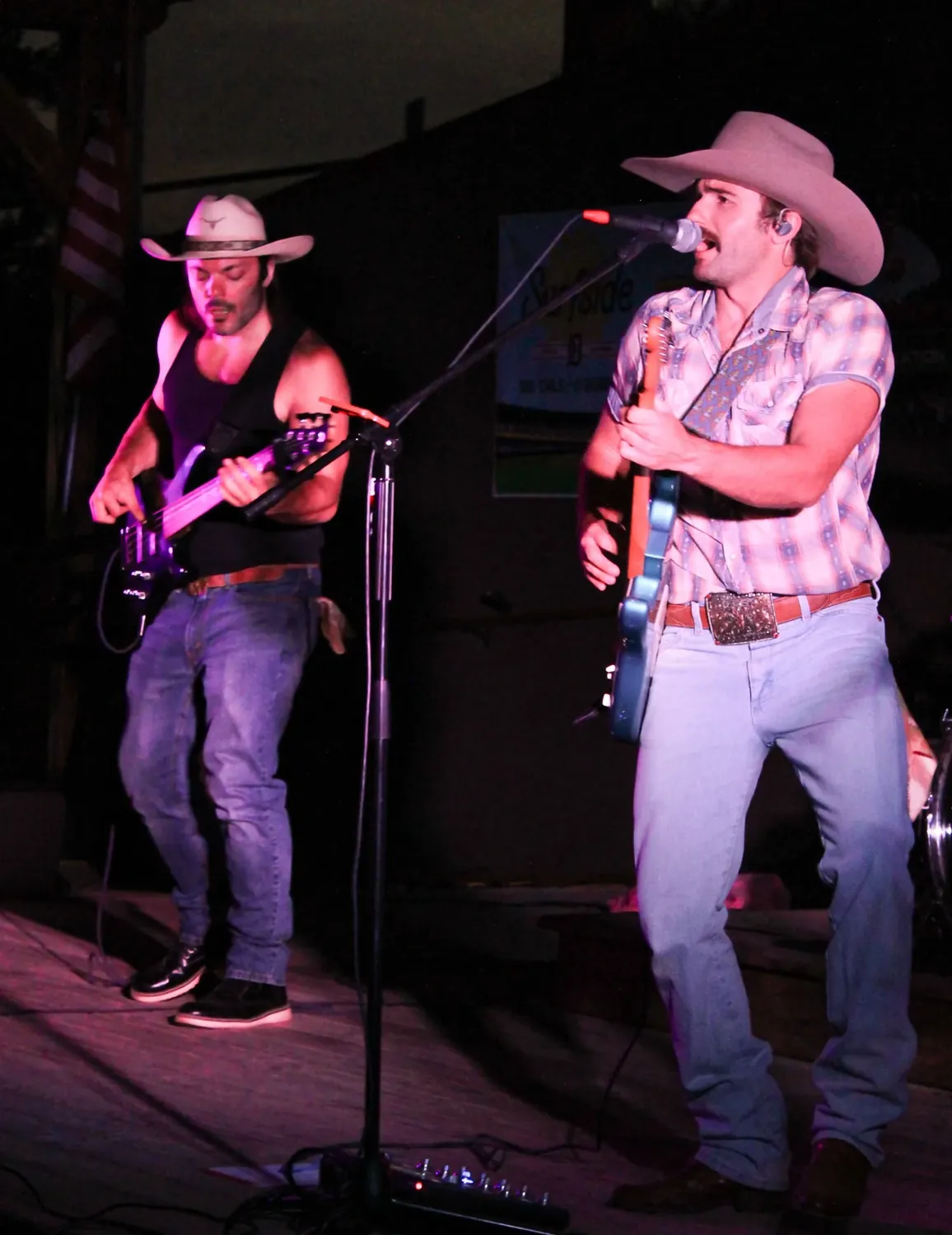 Two guitarists in cowboy hats singing and playing on the main stage under pink stage lights