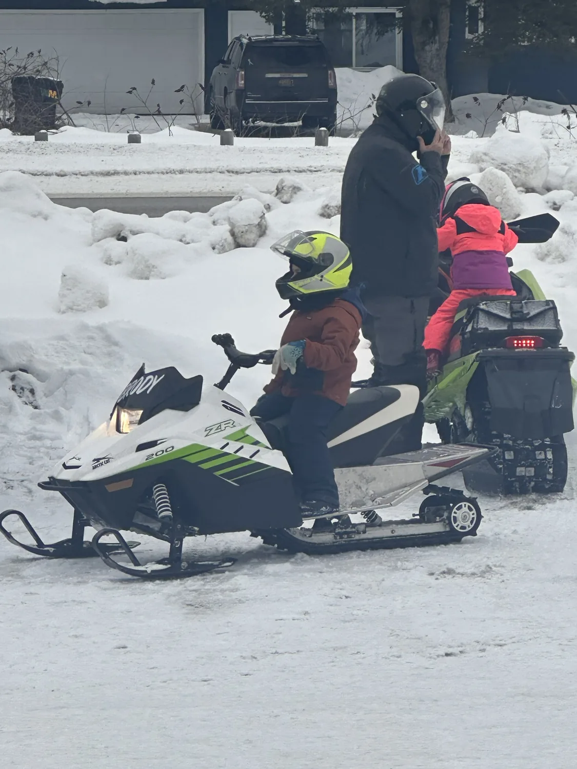 Family of snowmobilers in helmets on a youth Arctic Cat ZR 200 and full-size snowmobile in the snow