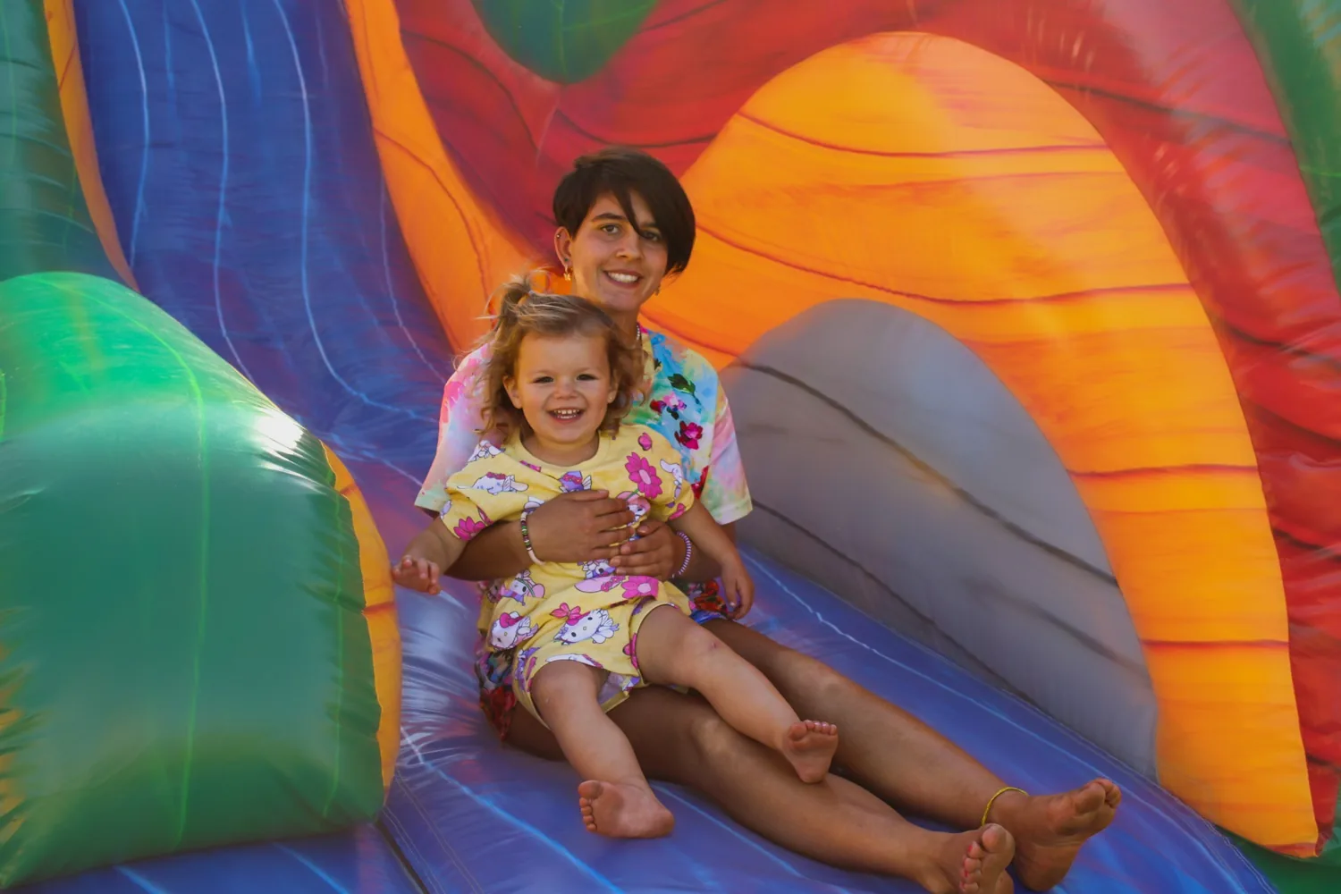Parent and smiling toddler going down the colorful inflatable slide at the 2nd Annual Harvest Festival