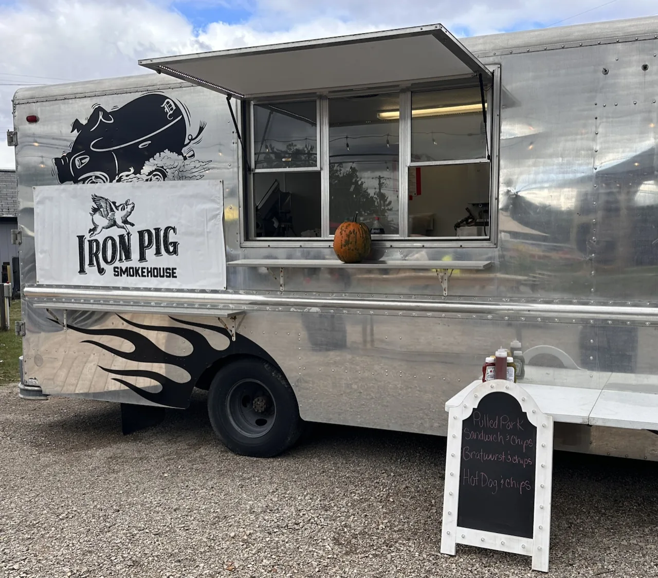 The Iron Pig Smokehouse food truck parked on the gravel patio with its serving window open and chalkboard menu sign