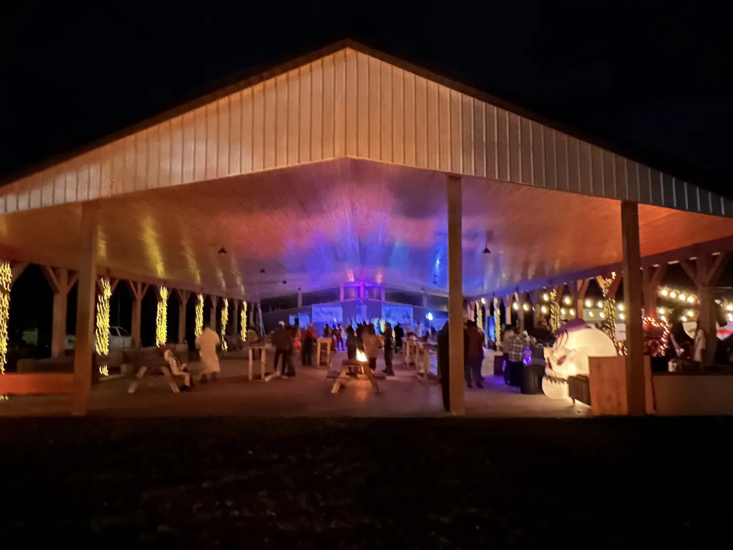 The covered pavilion lit up at night with warm string lights across the wooden rafters