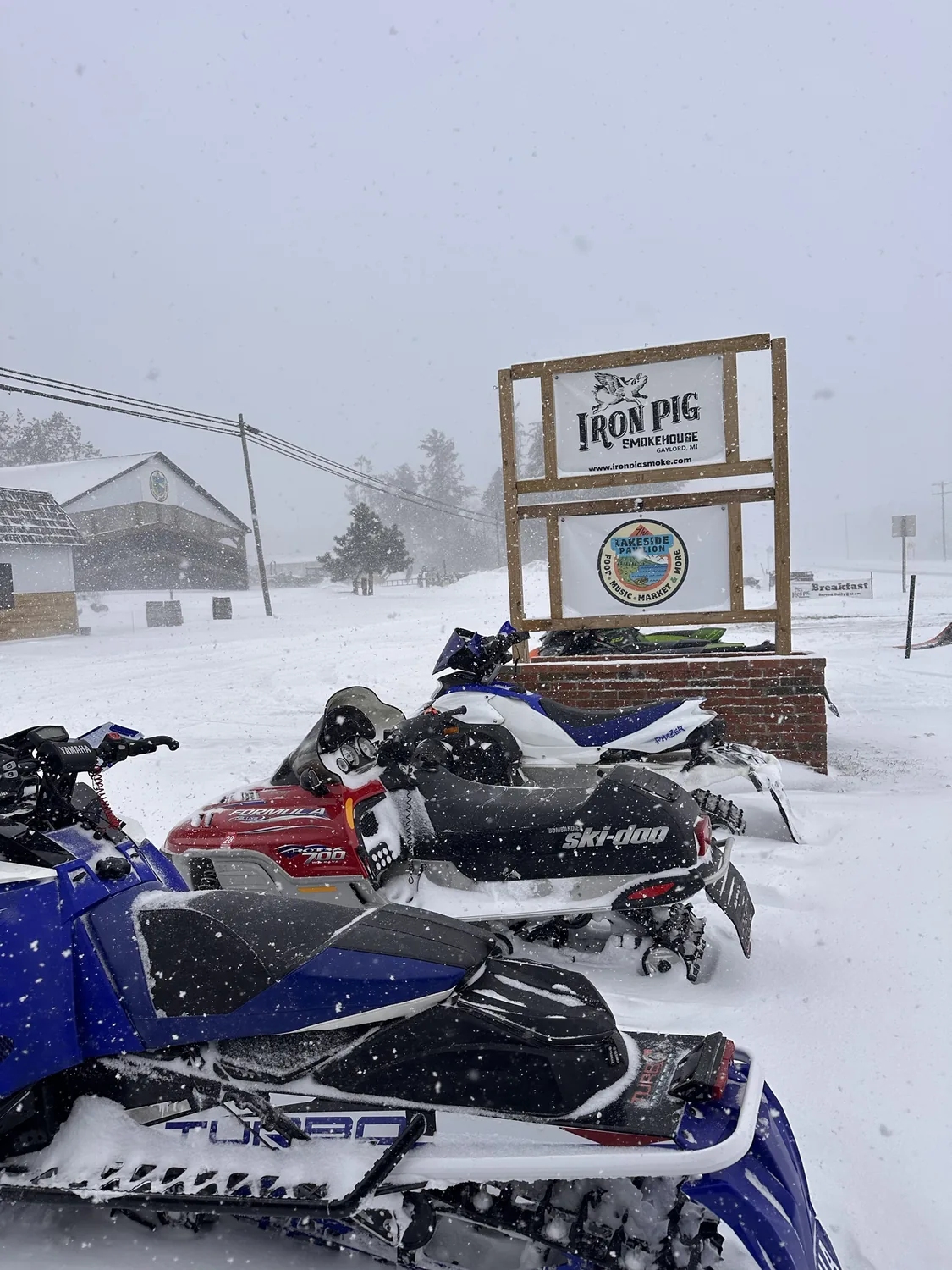 Snowmobiles parked in the snow in front of The Lakeside Pavilion sign in winter