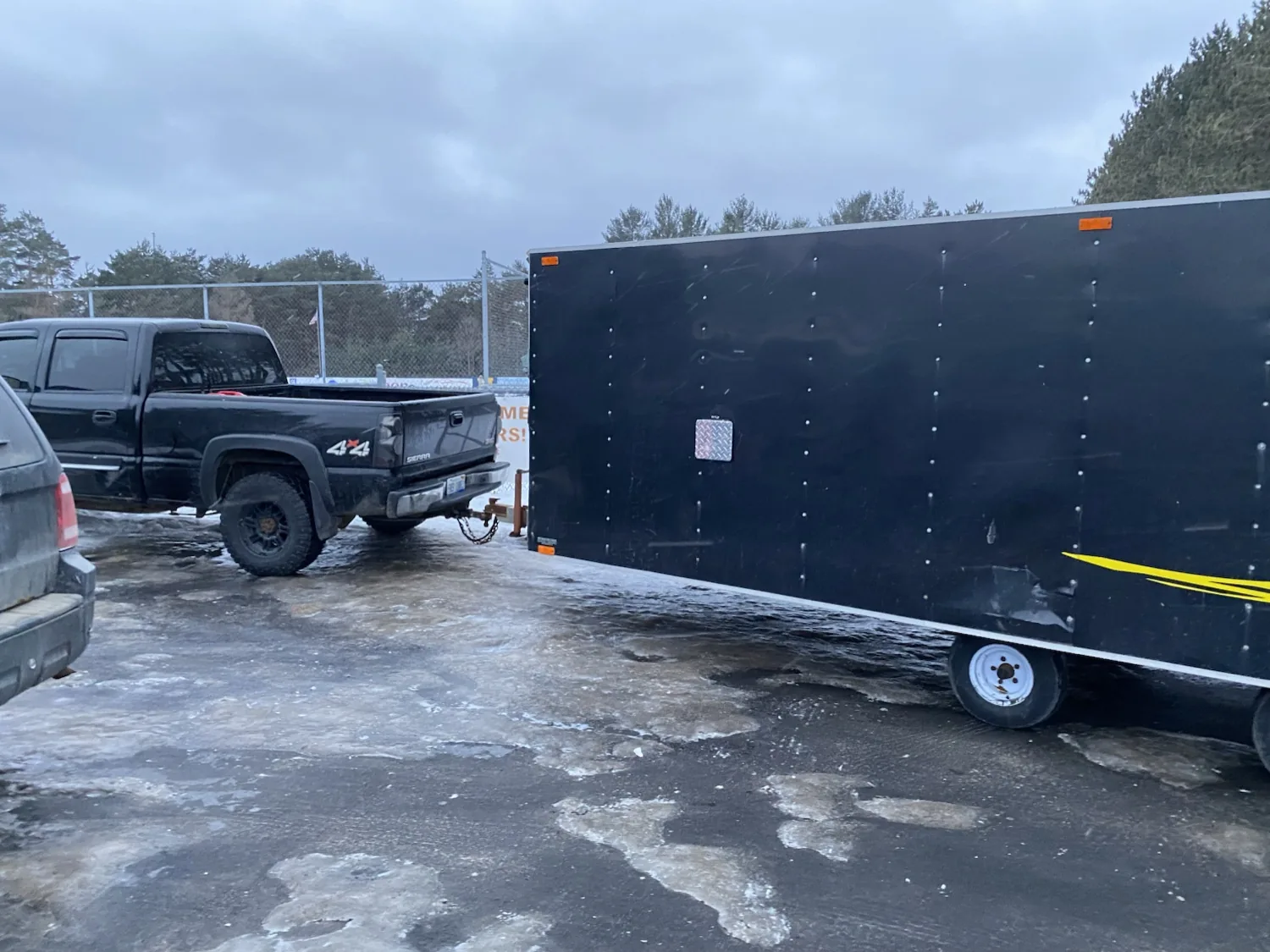 Pickup truck towing a large snowmobile trailer parked on site in winter