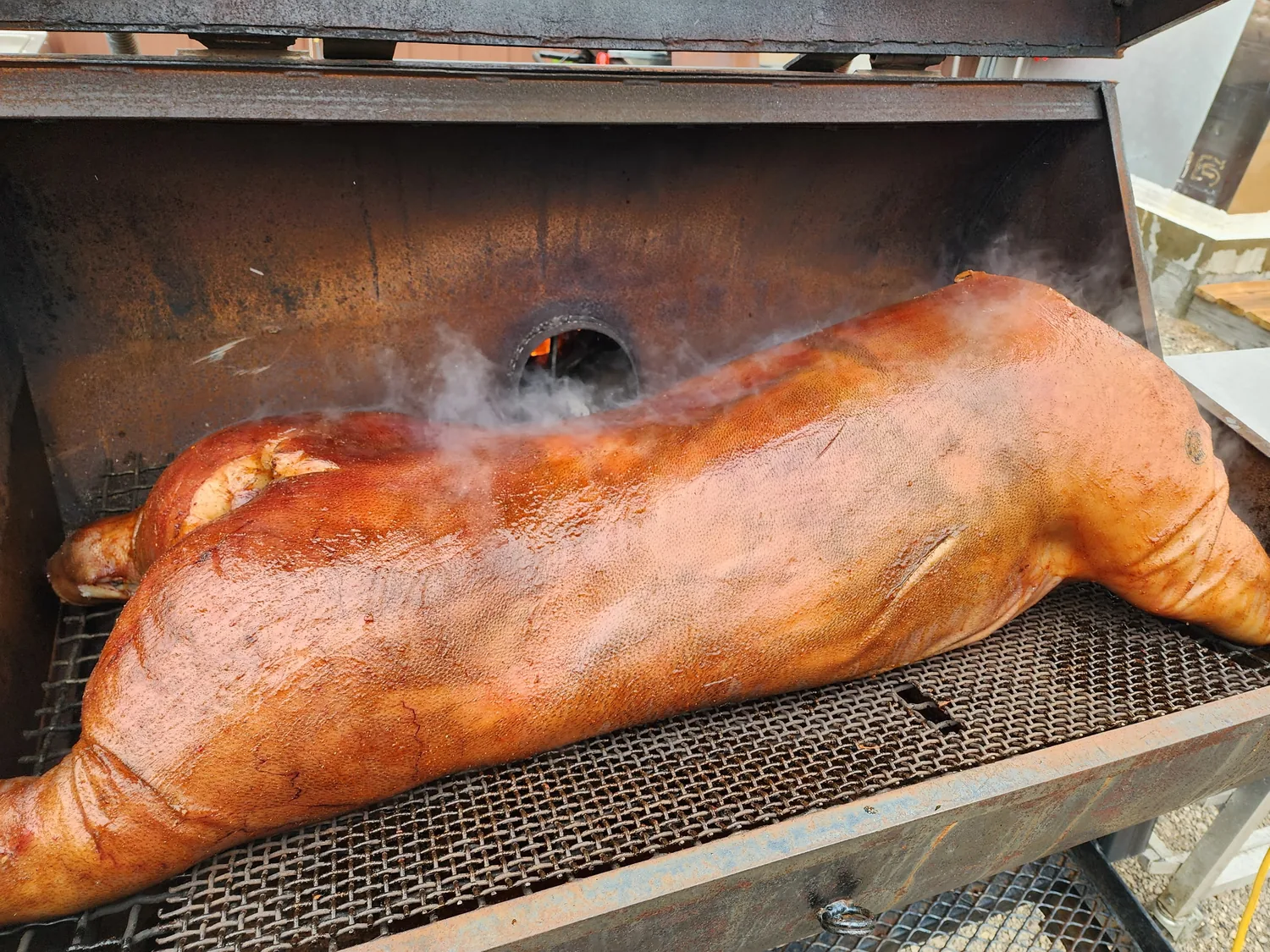 Whole hog smoking on the grates inside the Iron Pig Smokehouse offset smoker in the backyard at The Lakeside Pavilion